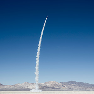 A rocket launches from a desert, leaving a smoke trail